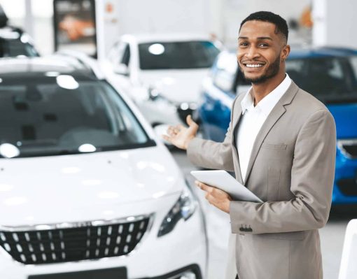 cheerful-car-dealer-gesturing-showing-brand-new-automobile-standing-indoors.jpg
